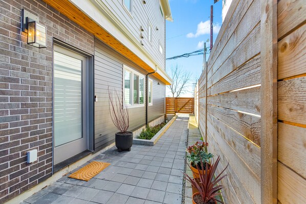 A narrow outdoor pathway with a wooden fence, a brick wall, and a modern building with a garage door.