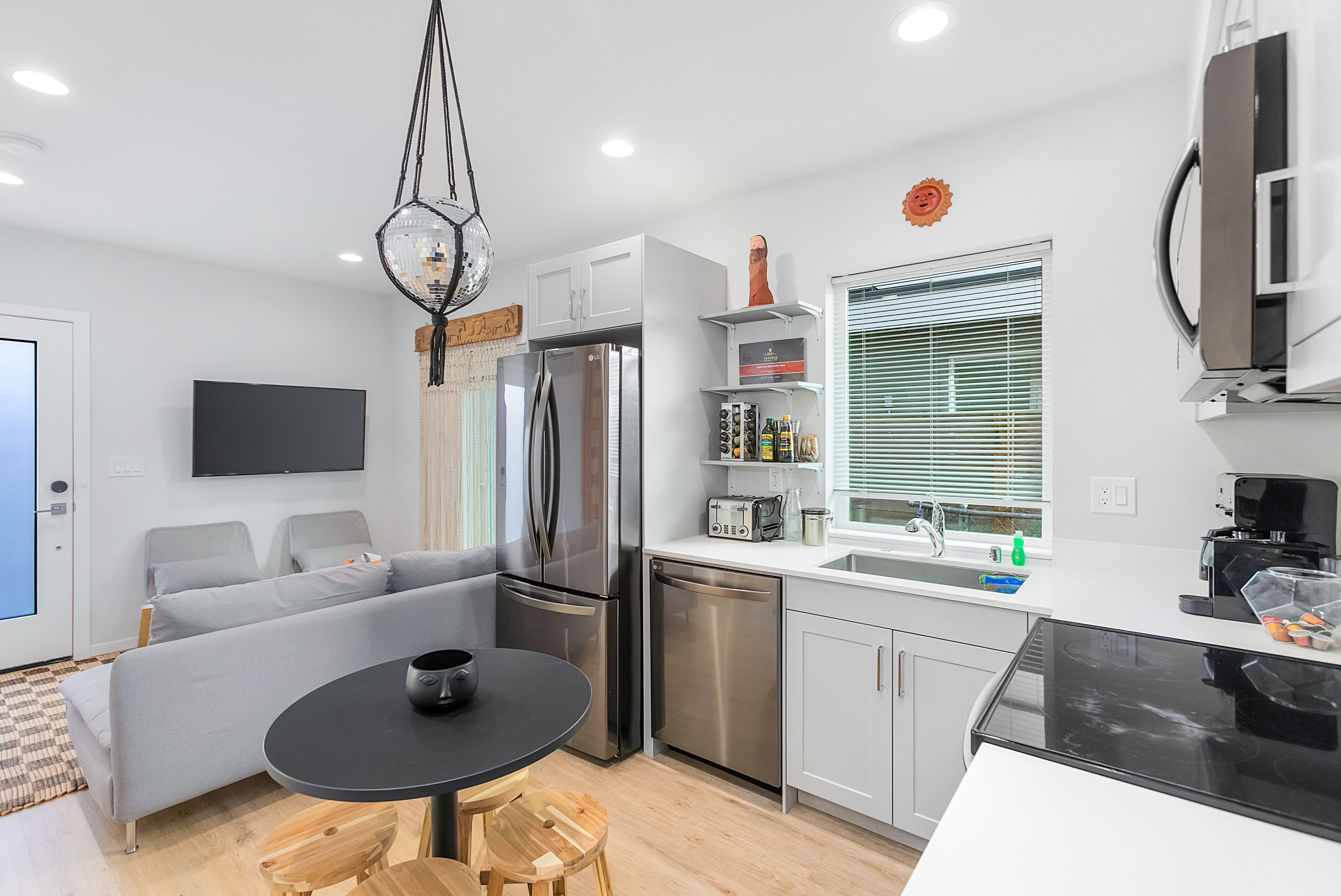 A modern kitchen with a black dining table, grey sofa, and stainless steel appliances.