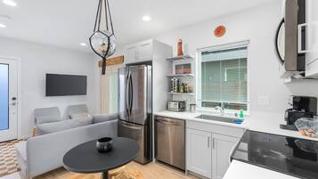 A modern kitchen with a black dining table, grey sofa, and stainless steel appliances.