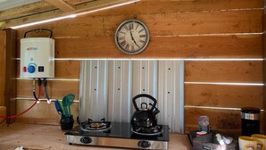 A kitchen with a gas stove, a kettle, a clock, and a water heater. - Mountain Quest Tipi (Rexford)