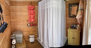 A compact wooden cabin room with a toilet, a small cabinet, a mirror, and a hanging rack with folded towels. - Mountain Quest Tipi (Rexford)