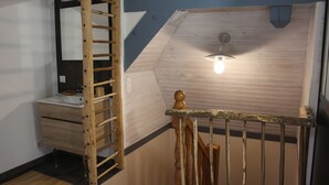 A staircase with a wooden handrail, a light fixture above, and a wooden wall with a white baseboard.
