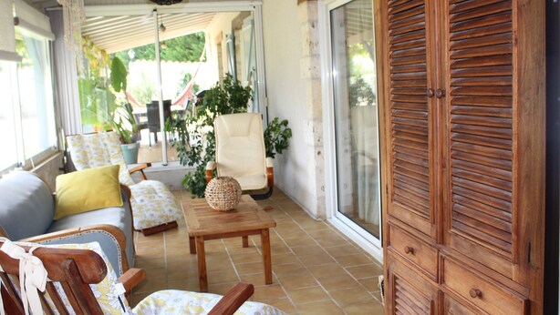 A sunlit patio with a wooden cabinet, a sofa with cushions, a chair, and a small table.