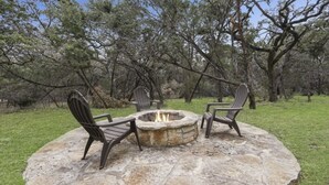 Ein Steine Feuerkorb mit zwei Adirondack-Stühlen in einer grünen Außenanlage, umgeben von Bäumen.