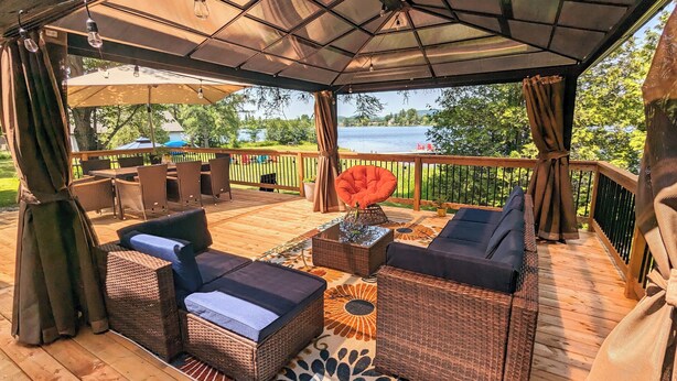 A covered outdoor seating area with wicker furniture, a central table, and a view of a lake.