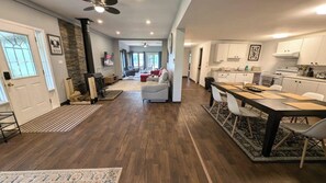 Una cocina moderna con armarios blancos, una zona de comedor con mesa oscura y una sala de estar con chimenea.
