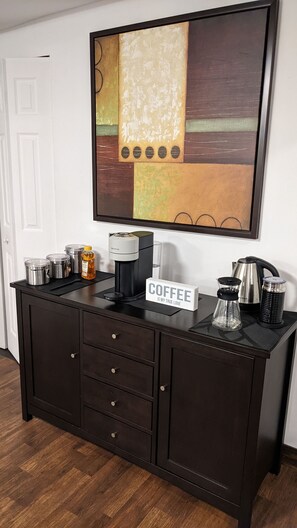 Un mueble de madera oscura con una cafetera, frascos y un cartel que dice 'COFFEE IS MY TRUE LOVE'.