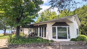 A small, single-story house with a covered porch, large windows, and a stone retaining wall.