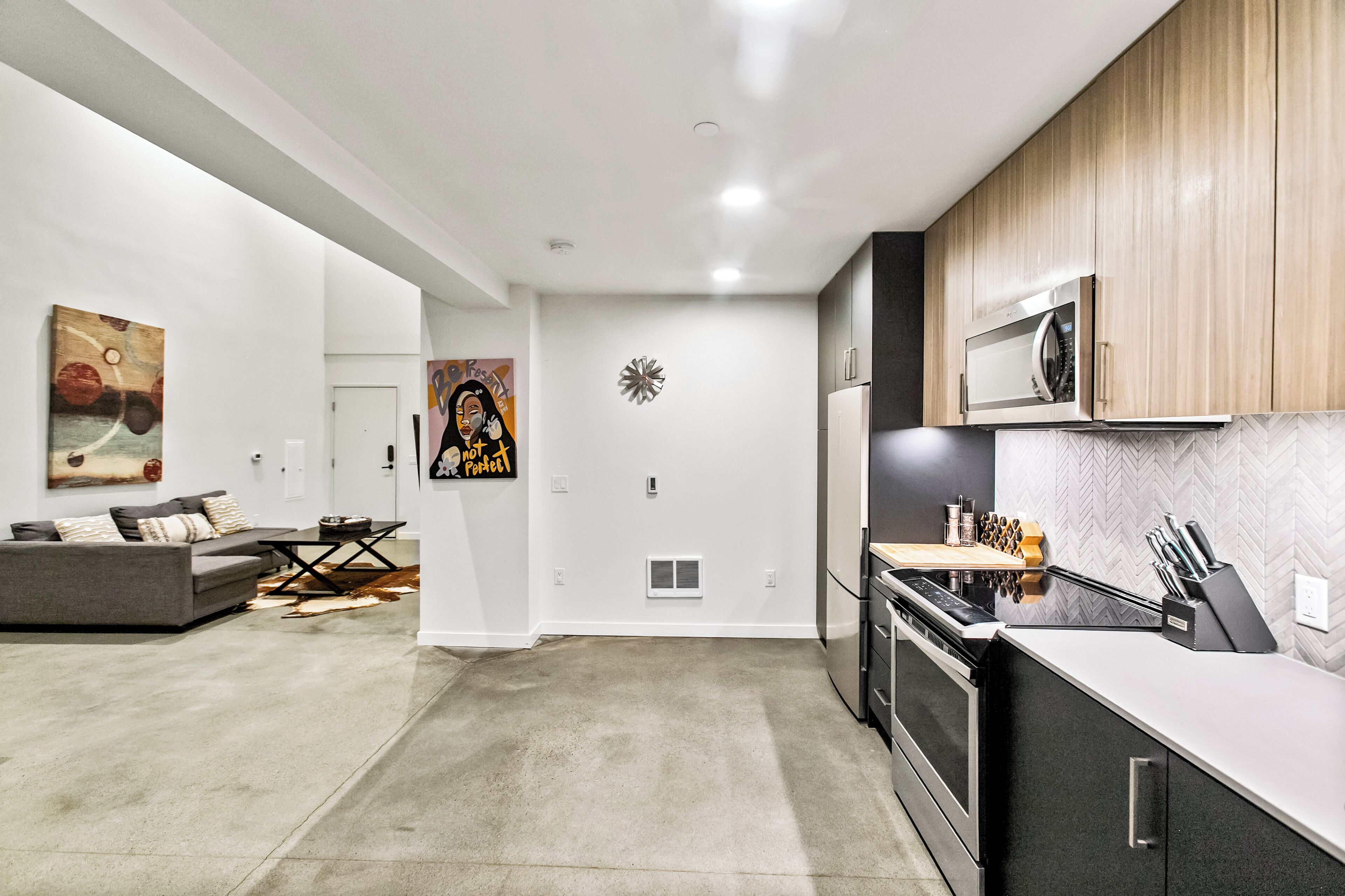A modern kitchen with a microwave, stove, and knife block. There is a dining area with a sofa and a coffee table.