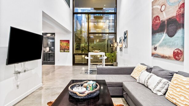 A modern living room with a flat-screen TV, a gray sofa, and a coffee table with decorative items. - Urban Loft in Redmond Core (Redmond)