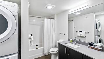 A modern bathroom with a built-in washer and dryer, a bathtub, a toilet, and a vanity with a mirror.