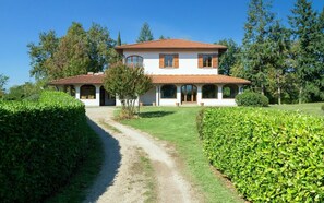 Ein zweistöckiges Haus mit Ziegeldach und weißen Wänden, umgeben von gepflegten Hecken und einem Kiesweg zum Eingang.