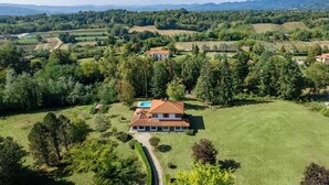 Uma casa de dois andares com piscina, cercada por vegetação exuberante e campos.