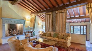 A cozy living room with a fireplace, comfortable seating, and large windows offering a view of the outdoors. - Villa Nocella - Private villa with pool in Tuscany (Dicomano)