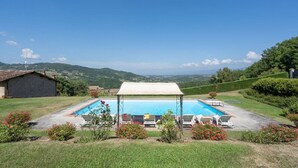 A rectangular pool with a canopy, surrounded by lounge chairs, in a grassy area with a view of hills. - Villa Nocella - Private villa with pool in Tuscany (Dicomano)