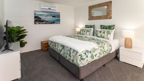 A bedroom with a bed, a TV, a plant, and a mirror on the wall. - Pheeney Place Five-star pet Friendly (Mallacoota)