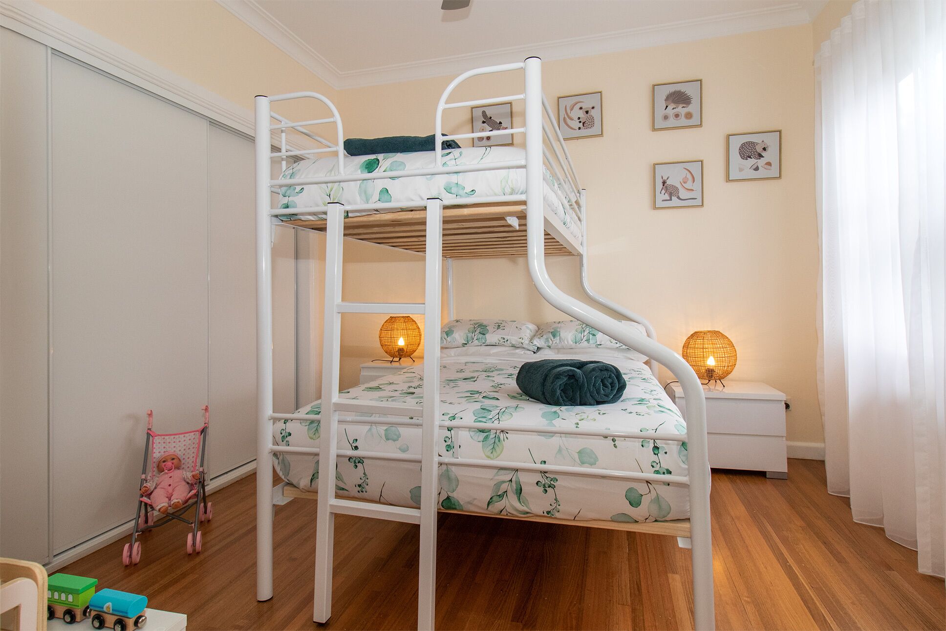 A bunk bed room with a floral bedspread, two bedside lamps, and a stroller.