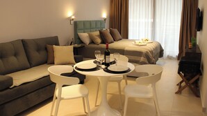 Et moderne hotelværelse med en sofa, et spisebord med stole, en seng med sengegavl og et fjernsyn på væggen.