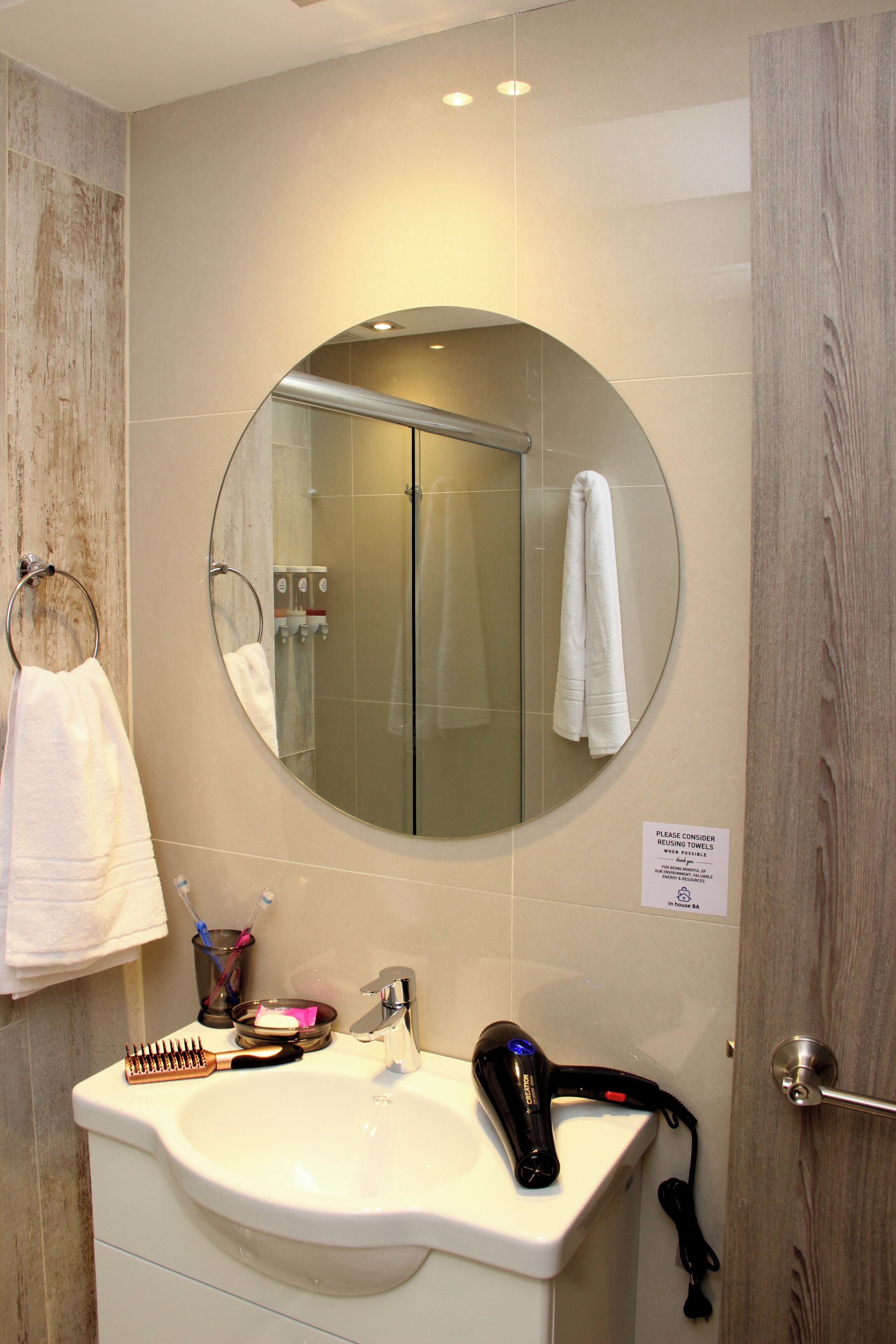 A bathroom with a round mirror, a sink, a towel rack, and a hairdryer.