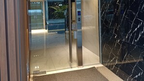 En moderne elevator med digitalt display, glasdør og en væg i marmor.