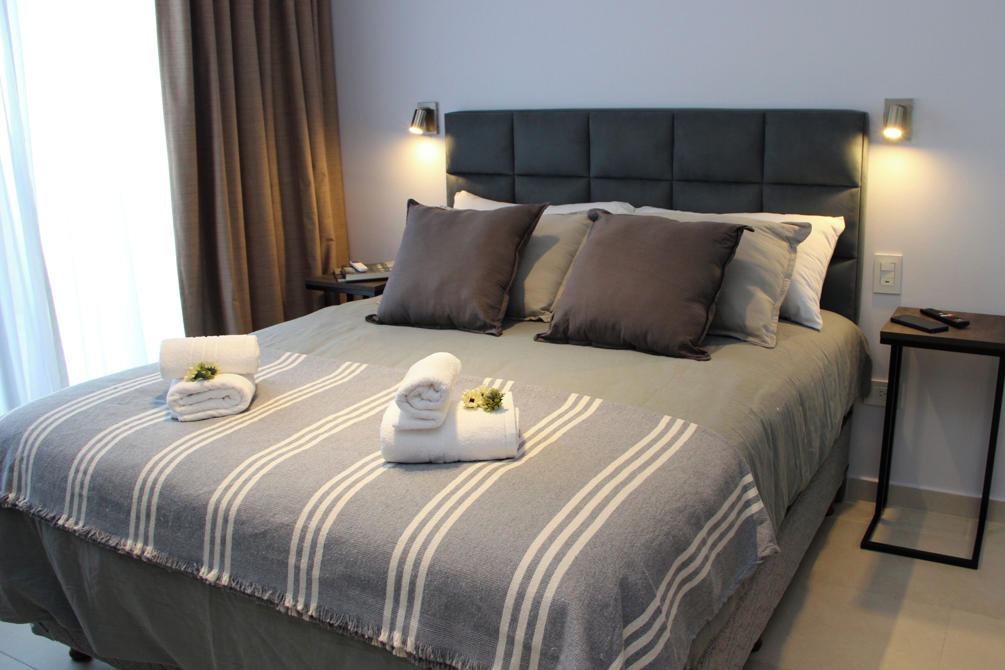 Una cama bien hecha con una colcha a rayas, dos almohadas y dos toallas enrolladas al lado.
