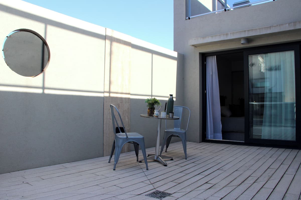 A balcony with two chairs and a small table, a round mirror, and a sliding glass door leading to an interior space.
