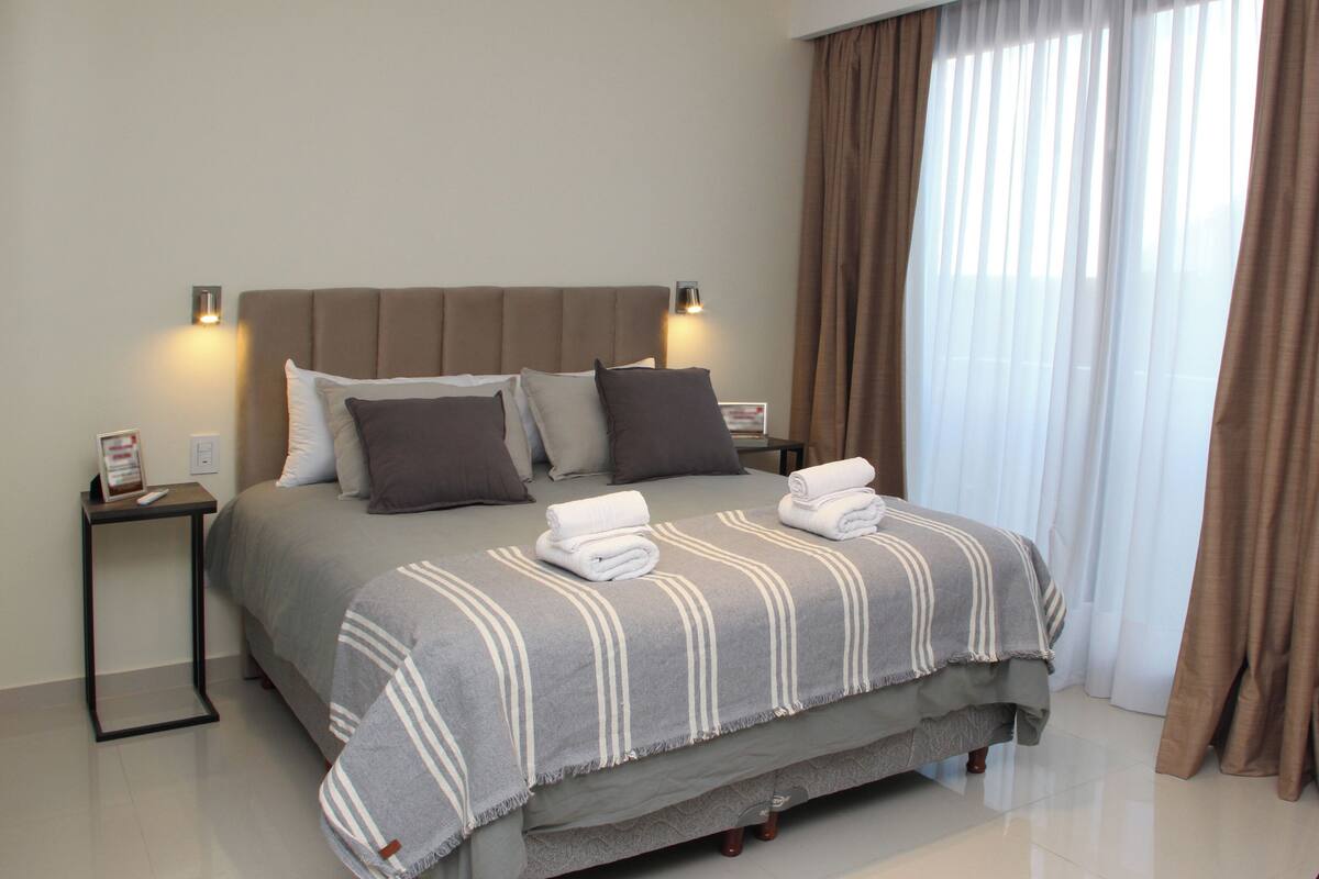 A neatly made bed with a striped blanket, two pillows, and two folded towels on a nightstand.