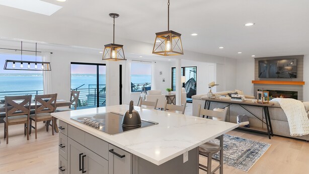A modern kitchen with a central island, pendant lighting, and a view of the sea.