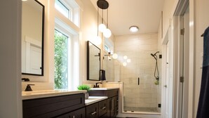 Een moderne badkamer met een grote spiegel, donkere meubels, een wastafel en een douche met glazen wand.