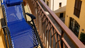 A balcony with a blue chair, a potted plant, and a view of the sea and buildings.