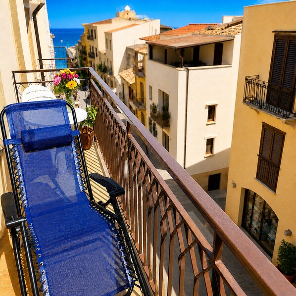A balcony with a blue chair, a potted plant, and a view of the sea and buildings.