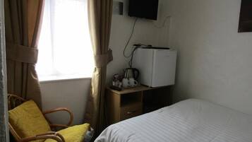 A hotel room with a bed, a wooden nightstand, a television mounted on the wall, and a window with curtains.