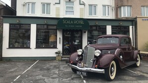 Een klassieke bordeauxrode auto geparkeerd voor Hotel Scala.