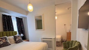 Een slaapkamer met een groot bed, een groene fauteuil, een klein tafeltje en een aan de muur bevestigde televisie.