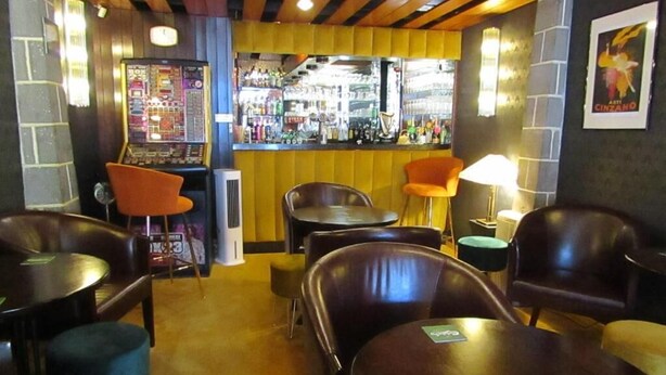 Een bar met houten plafond, barstoelen en een toonbank met diverse flessen.