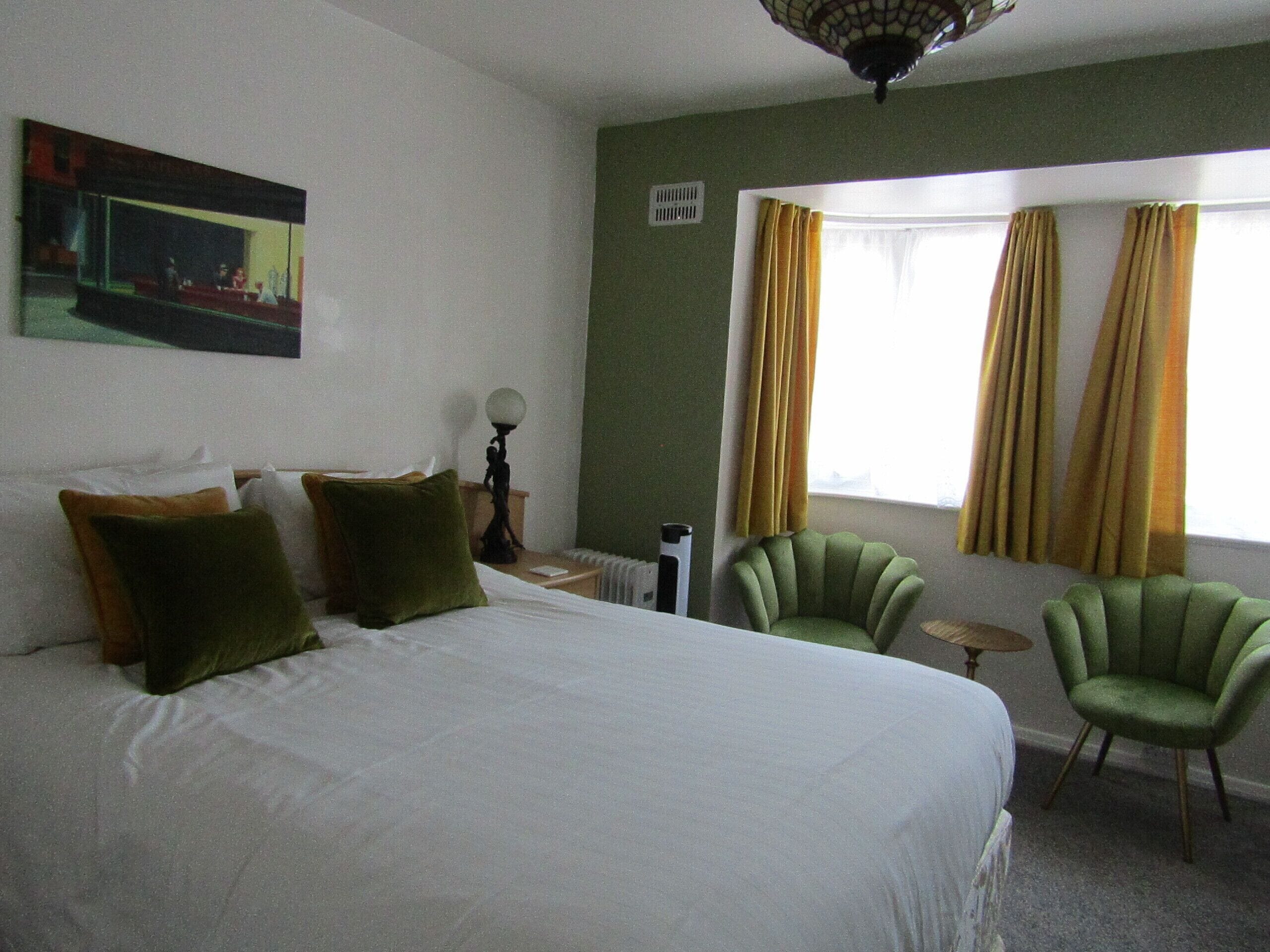 A hotel room with a large bed, two chairs, a small table, and a window with curtains.