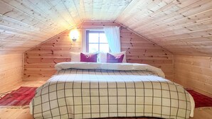 A cozy attic bedroom with a sloped ceiling, a bed with a plaid bedspread, and a window with curtains. - Cozy home in Reinli with sauna (Reinli)