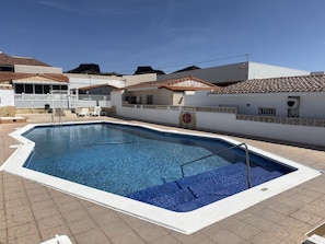 A rectangular swimming pool with a white border and a ladder, surrounded by a tiled deck.
