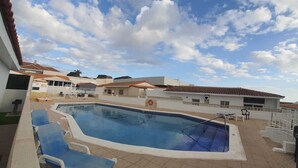 A swimming pool with lounge chairs, surrounded by buildings with tiled roofs.