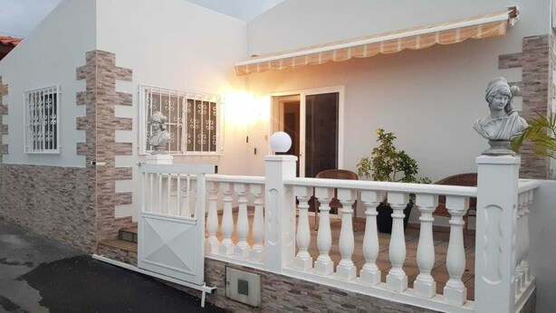 A modern house with a white exterior, stone accents, a balcony with white balustrades, and a statue on the right.