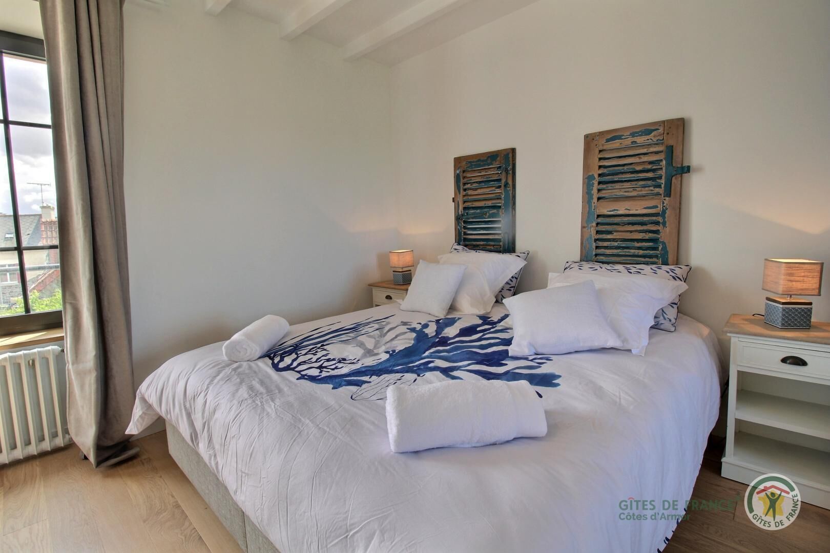 Une chambre à coucher avec un grand lit, deux lampes de chevet, une fenêtre avec des rideaux et un radiateur.