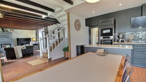 Un soggiorno moderno con un tavolo bianco grande, una scala, una cucina con forno a incasso e un orologio decorativo a parete.