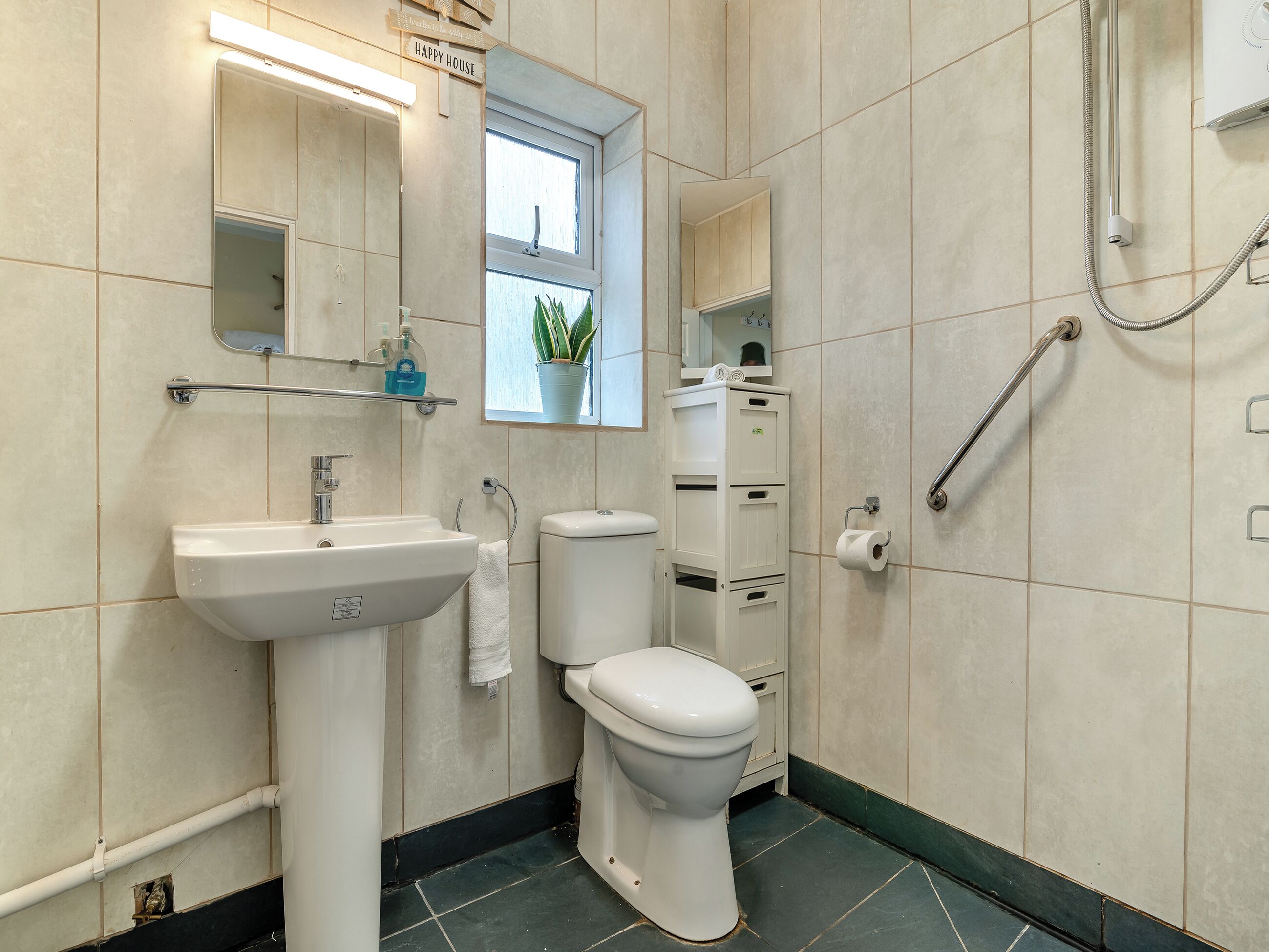 Ein modernes Badezimmer mit einem weißen Waschbecken, einer Toilette und einer Dusche. Über dem Waschbecken befindet sich ein Spiegel und über der Toilette ein Fenster.