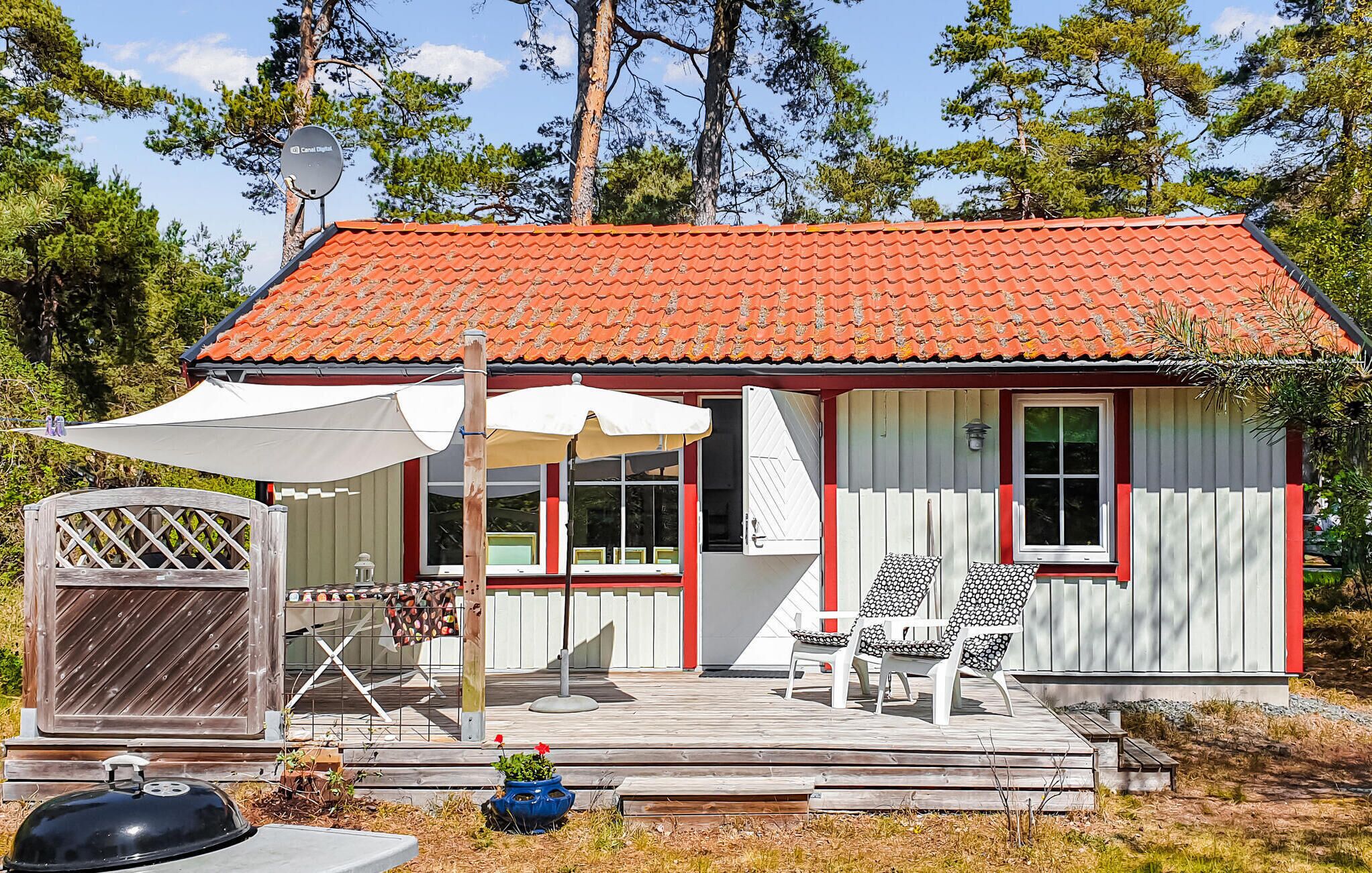 A small house with a red-tiled roof, a wooden deck, and a covered patio area with two chairs and a table.