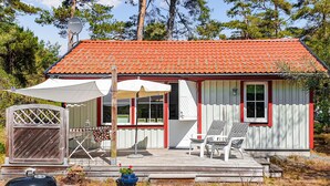 Pieni talo, jossa on punatiilinen katto, puinen terassi ja katettu patio, jossa on kaksi tuolia ja pöytä.