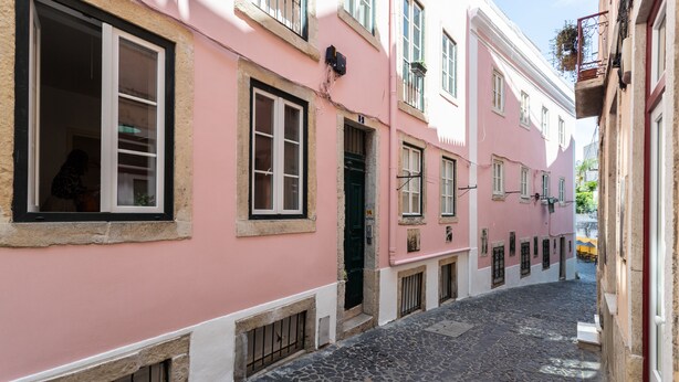 A narrow cobblestone street flanked by pink buildings with multiple windows and doors.