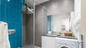 A modern bathroom with a glass-enclosed shower, a built-in washing machine, and a large mirror.