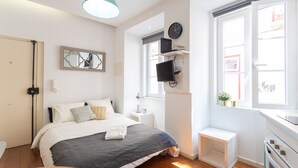 A modern bedroom with a bed, bedside table, TV, and a window with a view.