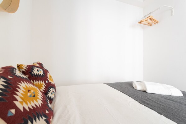 Una cama con un edredón blanco y gris, una manta colorida y una toalla blanca.