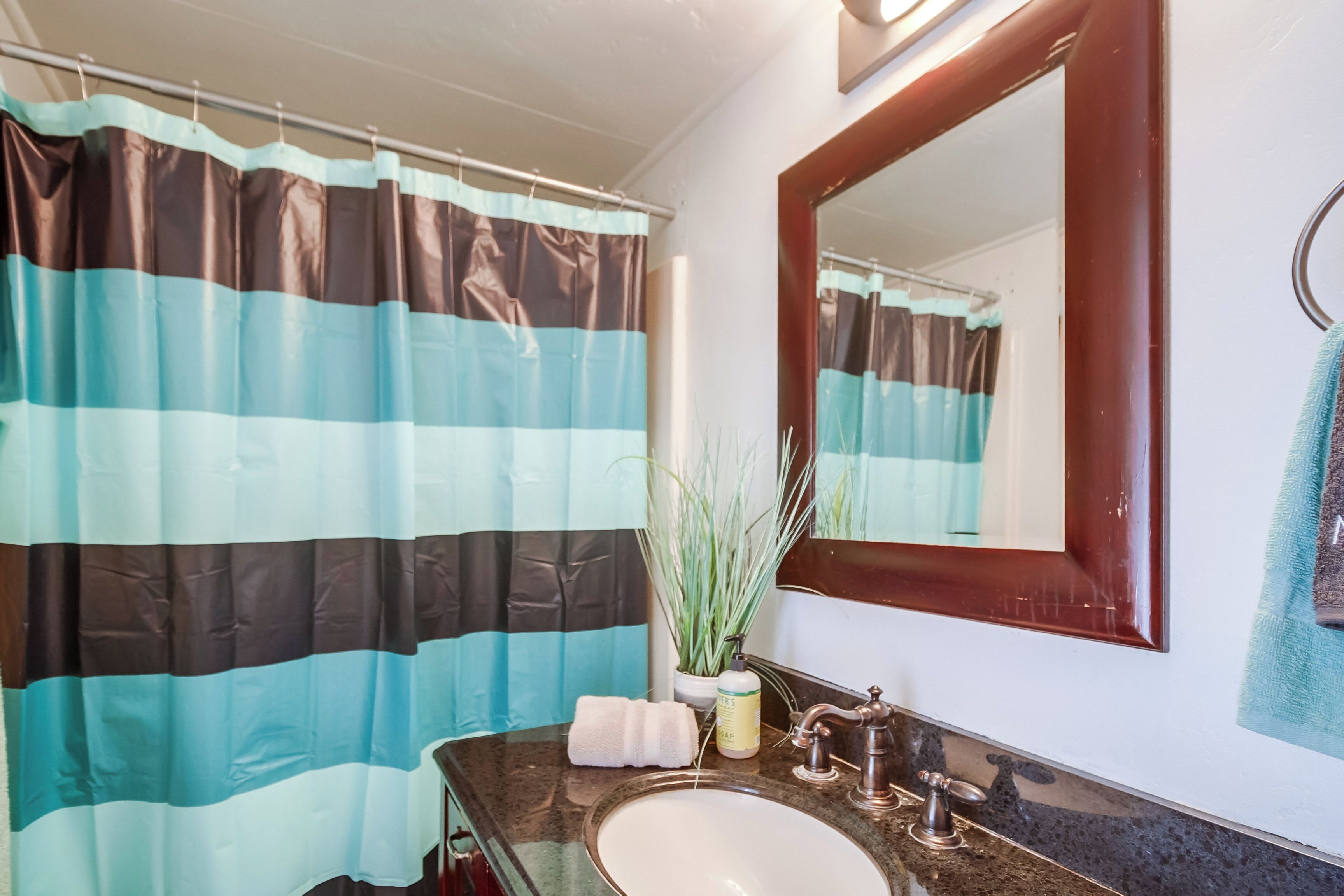 Een badkamer met een gestreept douchegordijn, een wastafel, een spiegel en een handdoekrek.